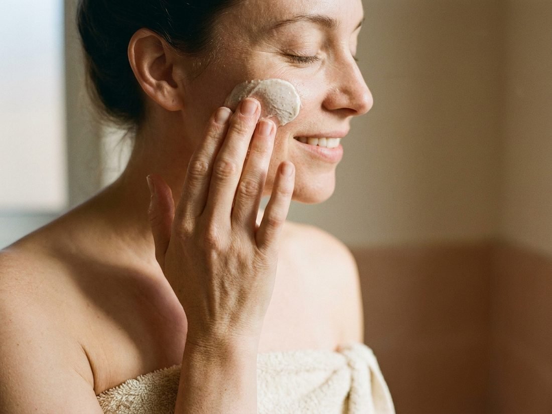 Close-up of a woman massaging a soft white creamy paste onto her cheek with her fingertips